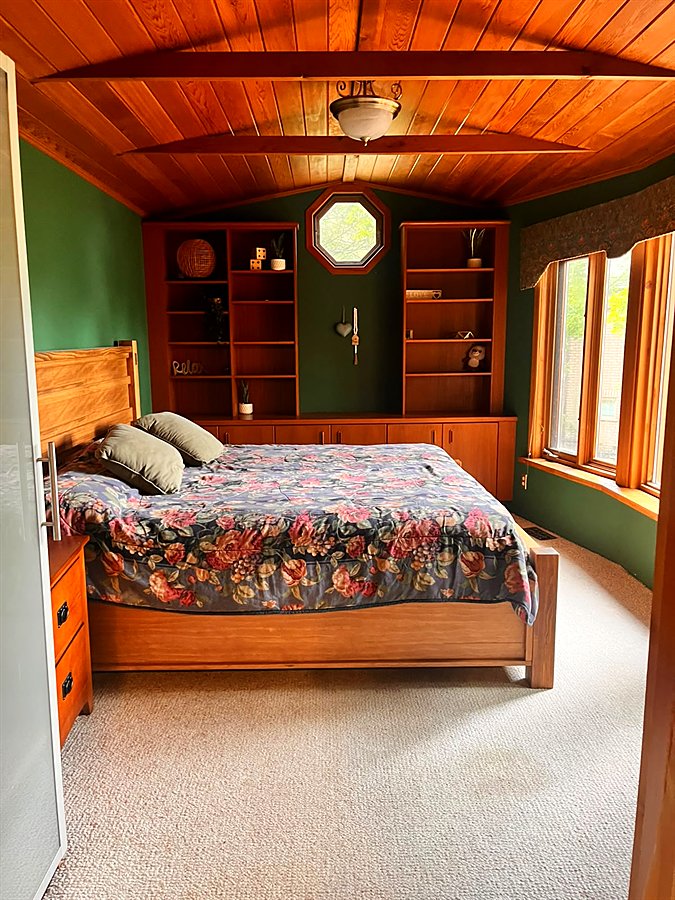 The green master bedroom with a king bed under a cedar ceiling and built-in wood shelves