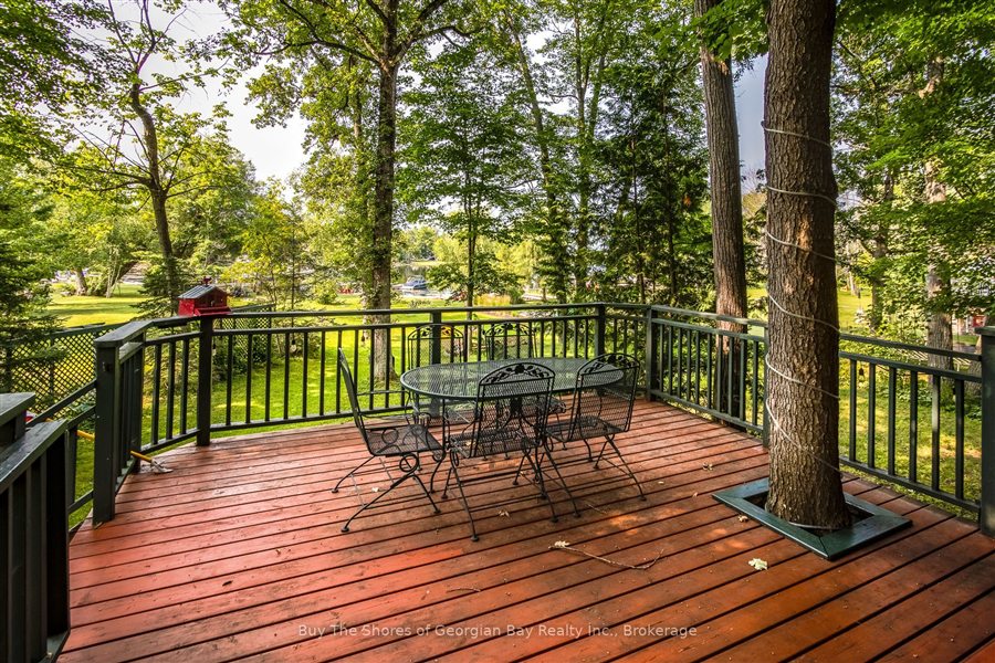 Deck table and chairs built around a tall tree, looking over the lawn