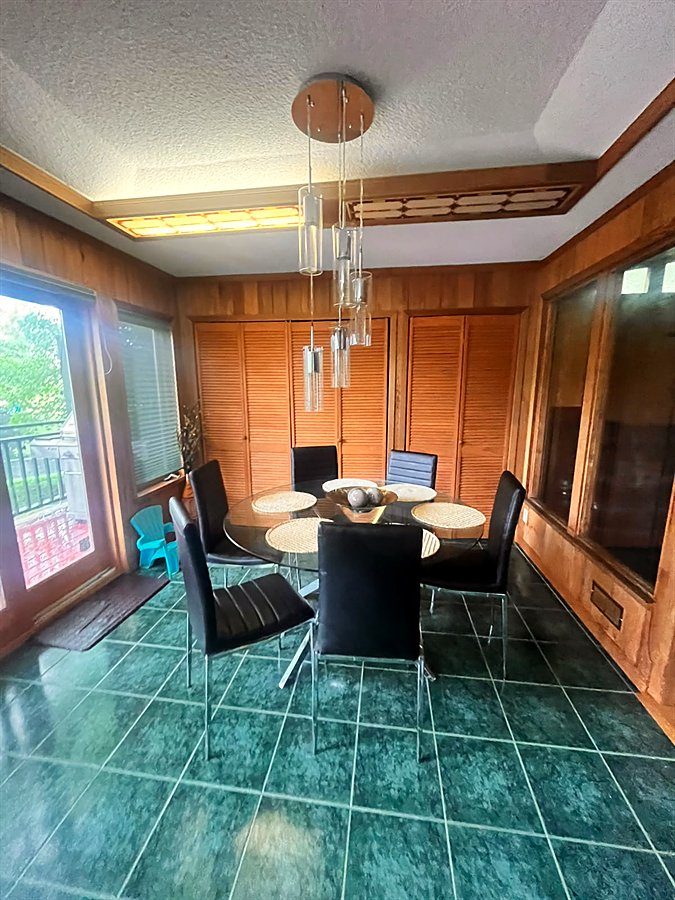 The dining table for six in the sunroom, under a hanging light with windows all around