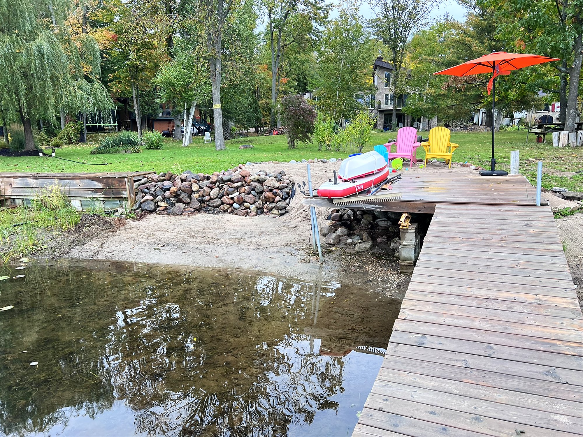 The private dock and sand beach, with a red umbrella and Muskoka chairs on the lawn