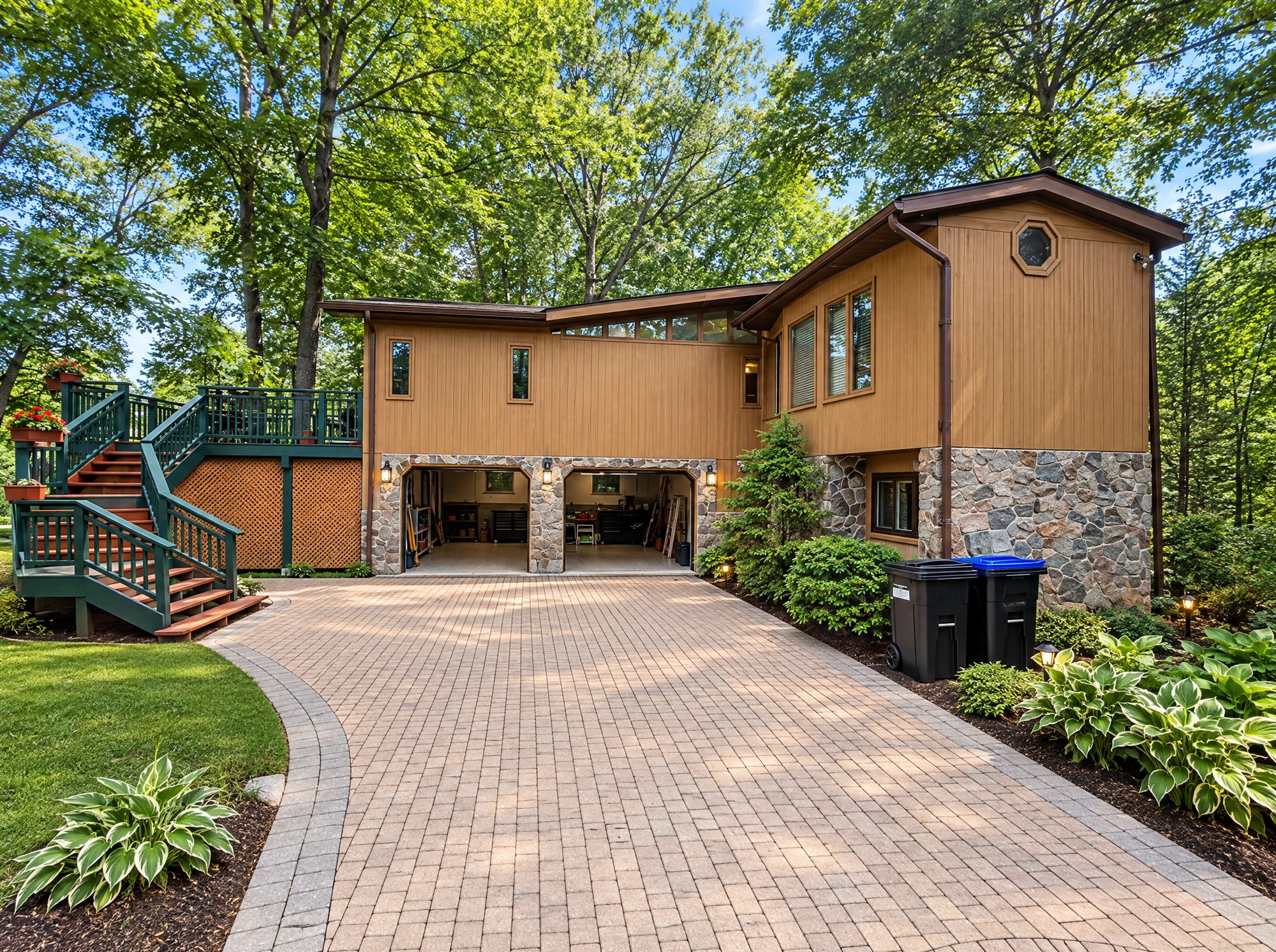 The cedar and stone house from the interlock drive, with the double garage and the stairs up to the raised deck